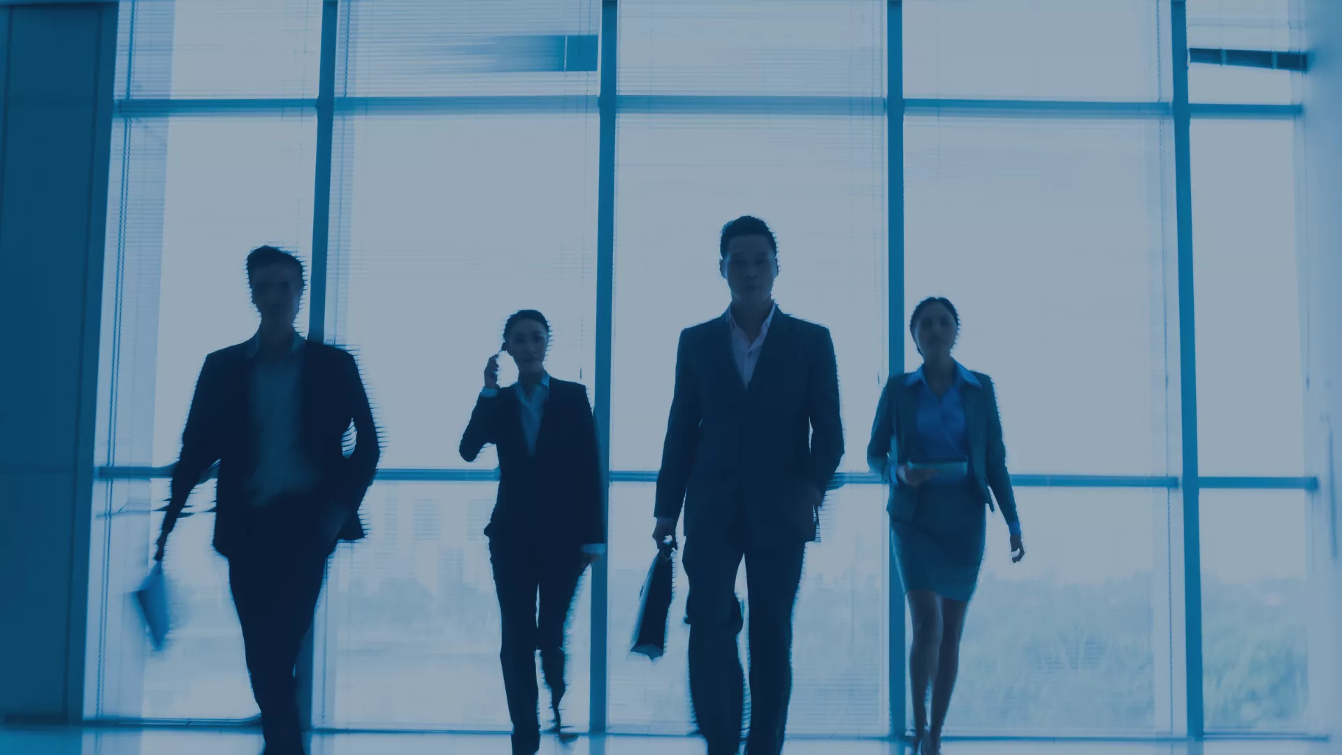 Fünf Business-Personen gehen entschlossen durch ein modernes Bürogebäude mit Glasfassade