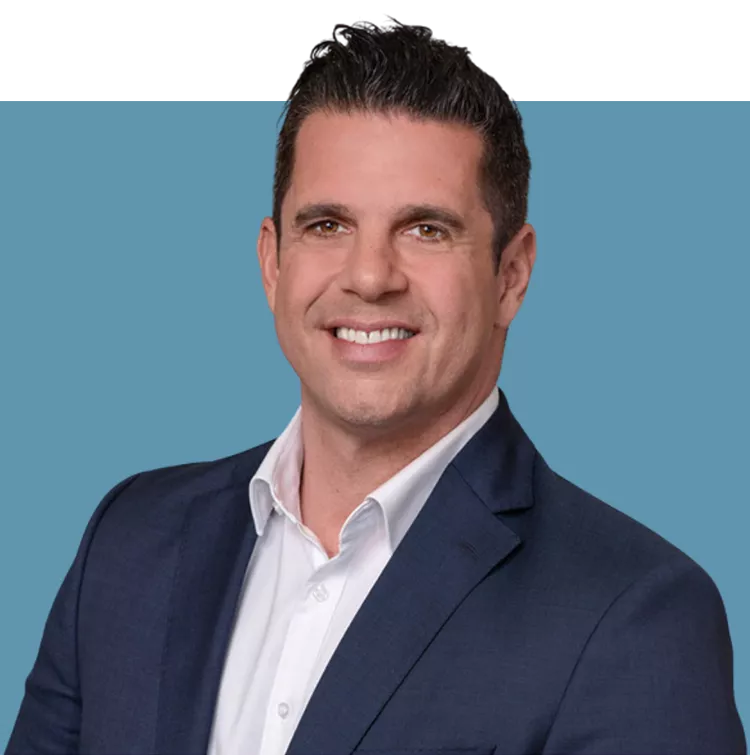 Porträt von Konstantin Tsaligopoulos, Vorstandsmitglied der audius SE, lächelnd in dunklem Sakko und weißem Hemd vor blauem Hintergrund.