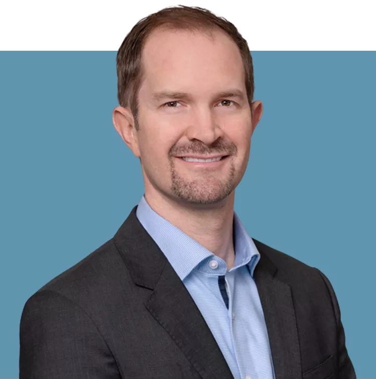 Porträt von Wolfgang Wagner, Vorstandsmitglied der audius SE, lächelnd in dunklem Sakko und blauem Hemd vor blauem Hintergrund.