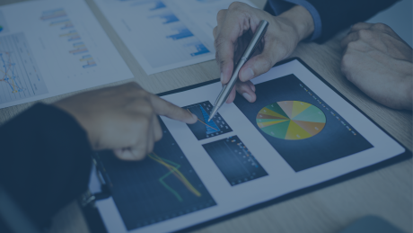 Zwei Personen analysieren gemeinsam Wirtschaftsdaten auf gedruckten Diagrammen und einem Tablet. Ein Kreisdiagramm und zwei Balkendiagramme stehen im Fokus. Der Kontext verweist auf wirtschaftliche Herausforderungen und die Chancen von Förderprogrammen, um digitale Prozesse wie ERP- und CRM-Systeme zu implementieren | audius